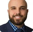 Smiling bald man with a beard wearing a dark suit and blue checkered shirt.